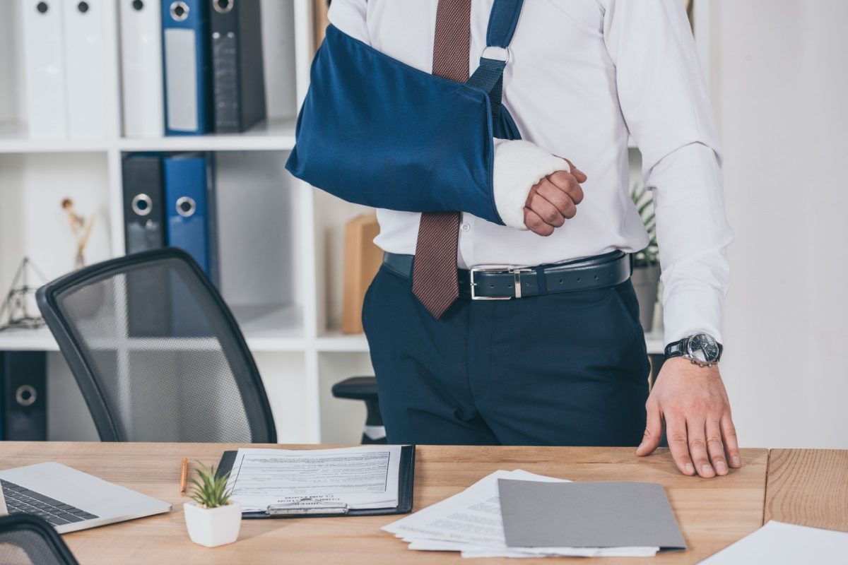 A worker with their arm in a sling standing at an office desk