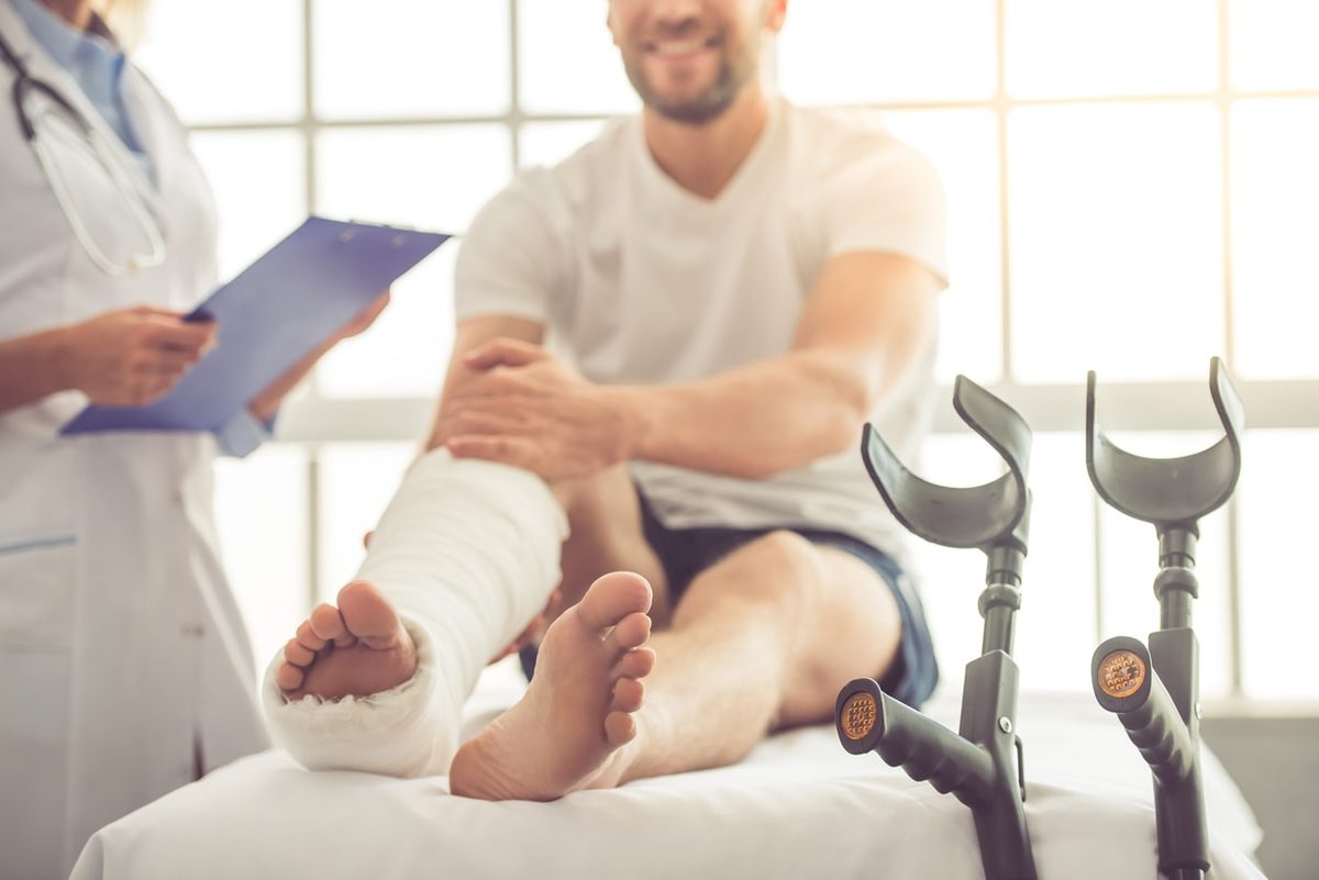 A person with a leg in a cast sitting with crutches beside a doctor