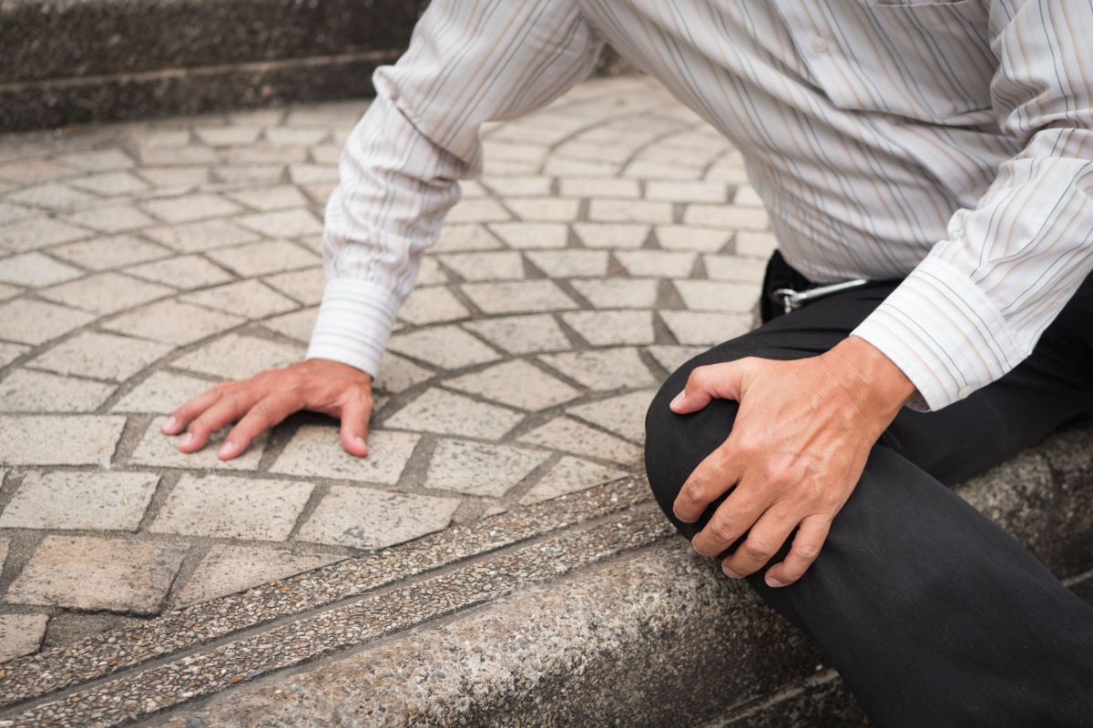 A person sitting on a pavement holding their knee after a fall