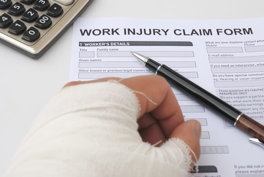 A bandaged hand completing a work injury claim form